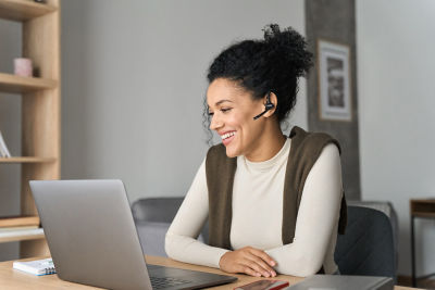 A person in a striped shirt and headscarf working on a laptop in a café.