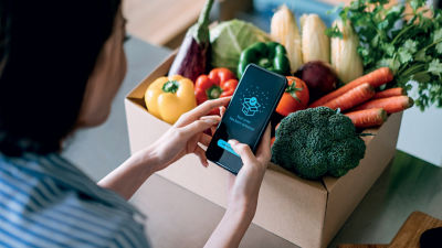 Woman with smartphone and vegetables in cardboard box