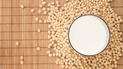 A glass of soymilk surrounded by soybeans with brown background