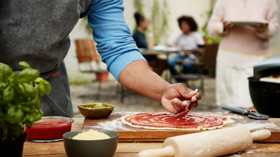 Un hombre le agrega salsa de tomate a una pizza