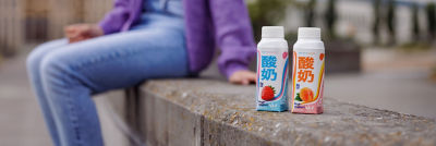 Drinking yoghurt in Tetra Top cartons, young woman sitting on stone bench