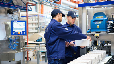 Operadores Tetra Pak inspecionam tabuleiro com embalagens de cartão