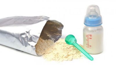 A filled infant formula bottle next to a bag of whey