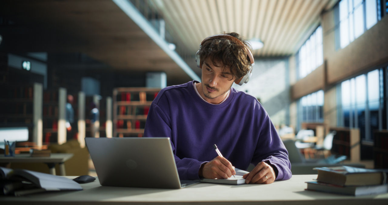 Thoughtful Young Student Preparing for Class, Doing Homework on a Laptop Computer. Freelance Journalist Working on an Article in a Public Library with Modern Simple Interior