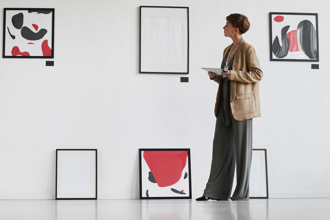 Full length portrait of creative elegant woman looking at paintings hanging on white wall while visiting modern art gallery exhibition, copy space