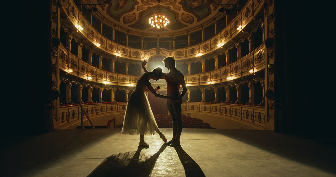 Cinematic shot of Young Couple of Classical Ballet Dancers Performing on the Stage of Classic Theatre with Dramatic Lighting. Male and Female Dancers Rehearse their Performance Together Before a show