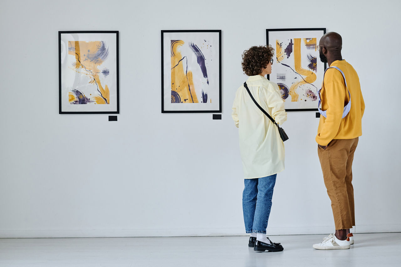 Rear view of young couple visiting art gallery, they standing and watching modern art
