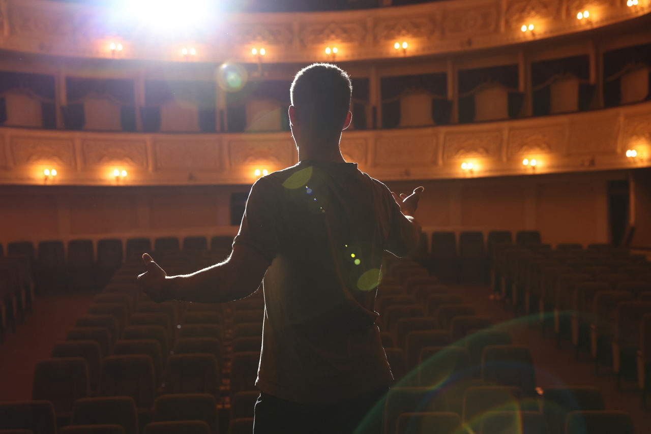 Professional actor rehearsing on stage in theatre, back view