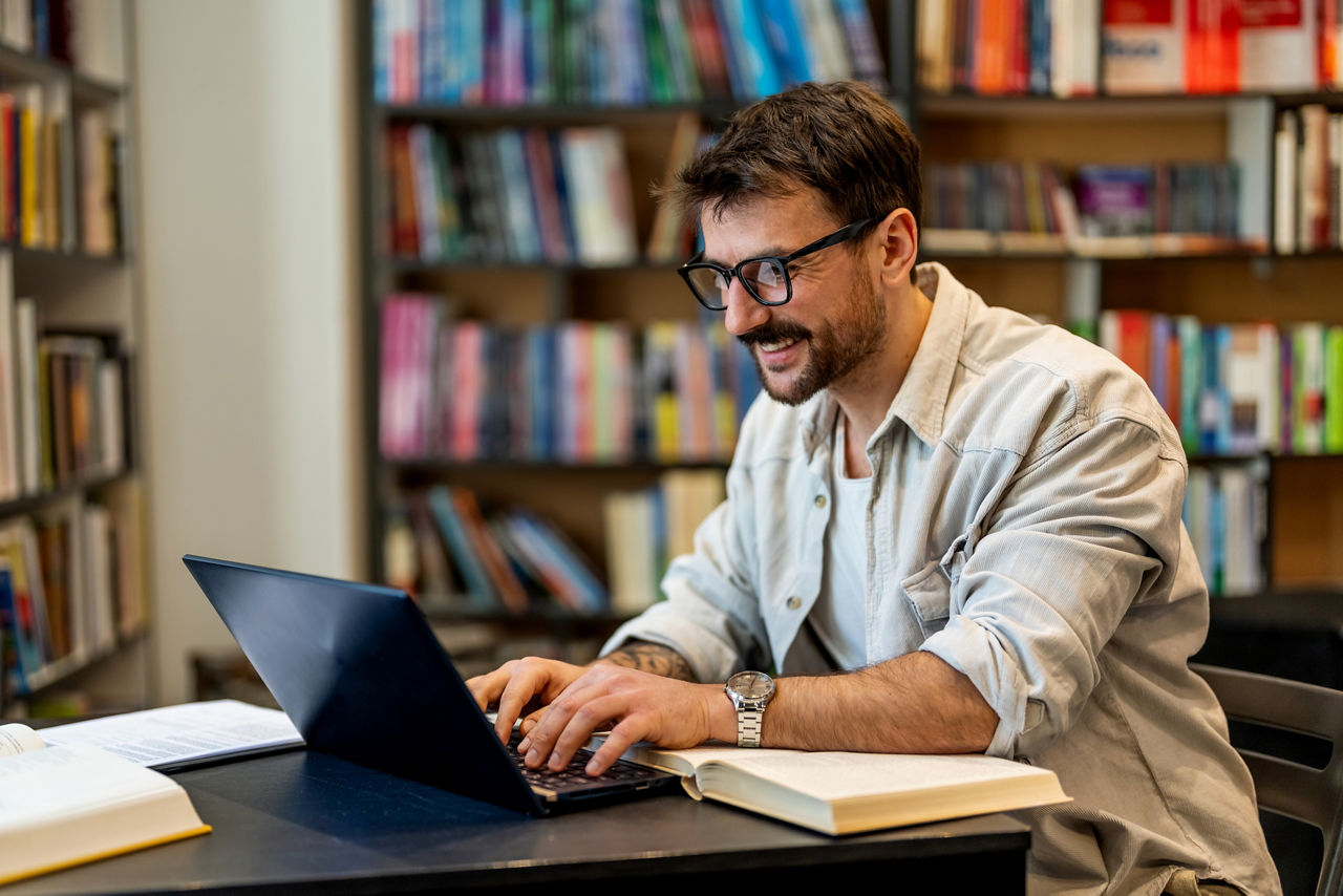 Handsome male student in a university library working on laptop. Young man studying on school assignment.