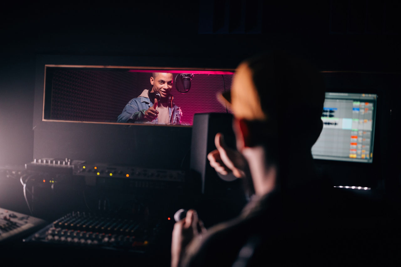 Young hipster African American pop singer recording songs with music producer in music studio