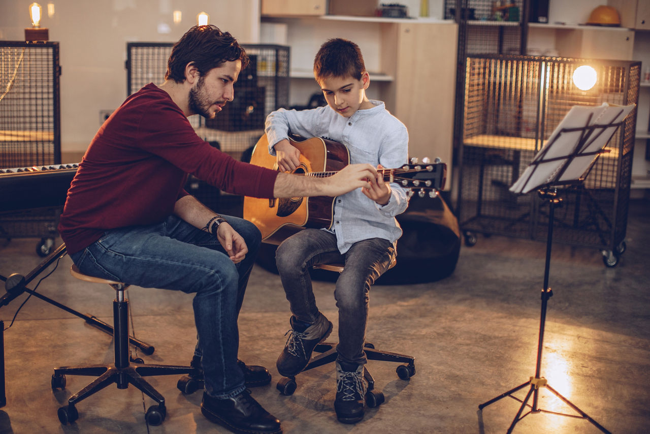 Two people, man guitar teacher working with little boy on guitar lessons.