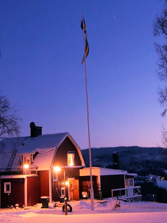 Et indbydende oplyst svensk hus i et vinterlandskab ved aftentide.