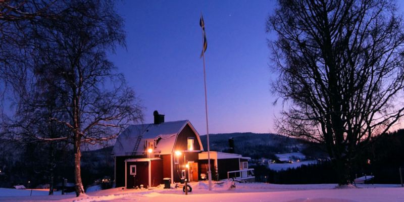 Ein einladend erleuchtetes Schwedenhaus steht in einer abendlichen Winterlandschaft.