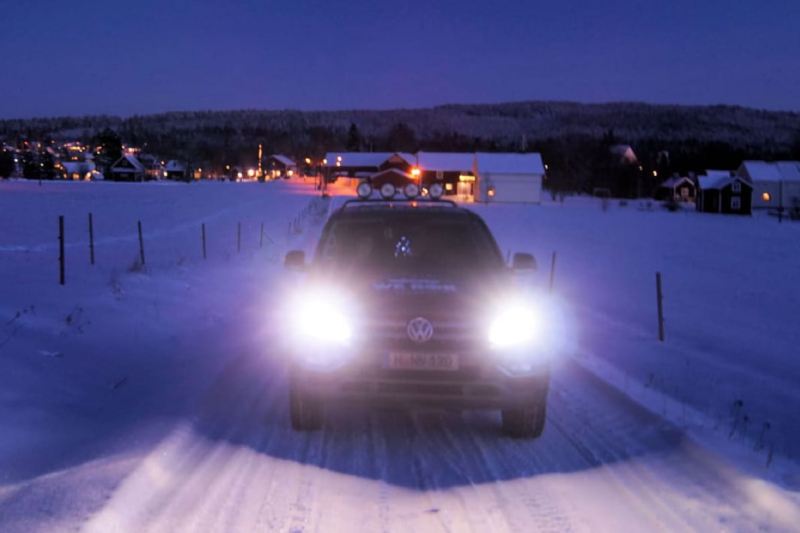 Ein Amarok mit leuchtenden Scheinwerfern fährt abends eine verschneite Straße entlang.
