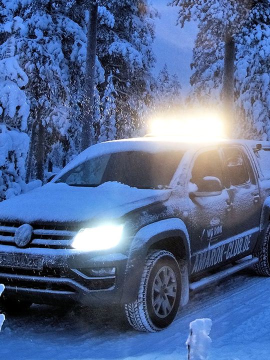 Der Volkswagen Nutzfahrzeuge Amarok fährt bei Dämmerung durch eine verschneite Winterlandschaft.