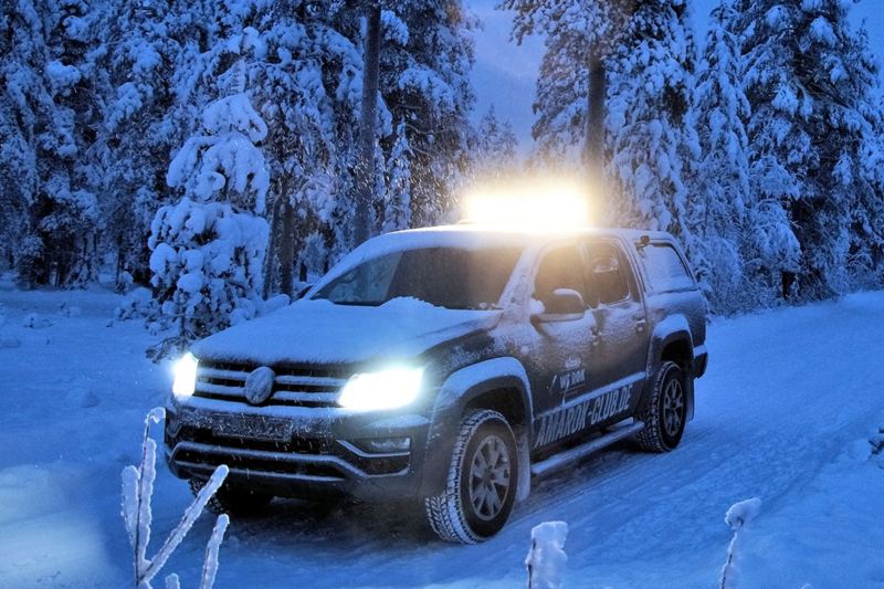 En Amarok fra Volkswagen Erhvervsbiler kører gennem et sneklædt vinterlandskab ved skumringstid.