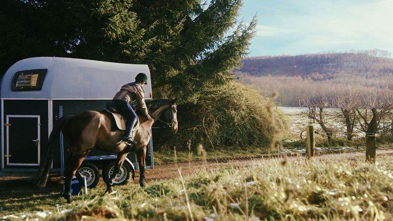 Janina Sandvoß on her horse rides past her horse trailer