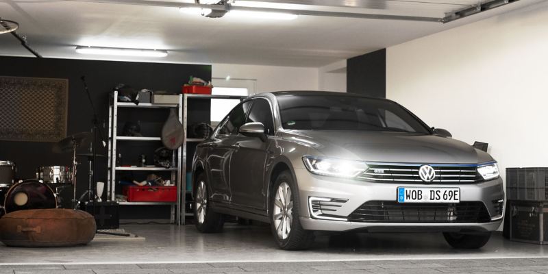 Father's new silver Passat GTE with glowing headlights parks in the garage