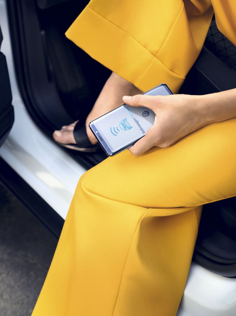 Piernas de una mujer con pantalones amarillos saliendo de un T-Cross con un móvil en la mano