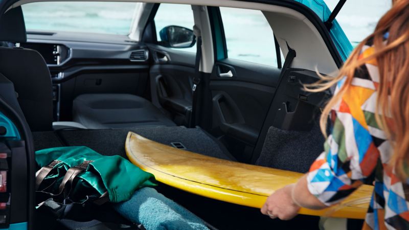 Chica introduciendo una tabla de surf en el interior de un T-Cross a través del maletero