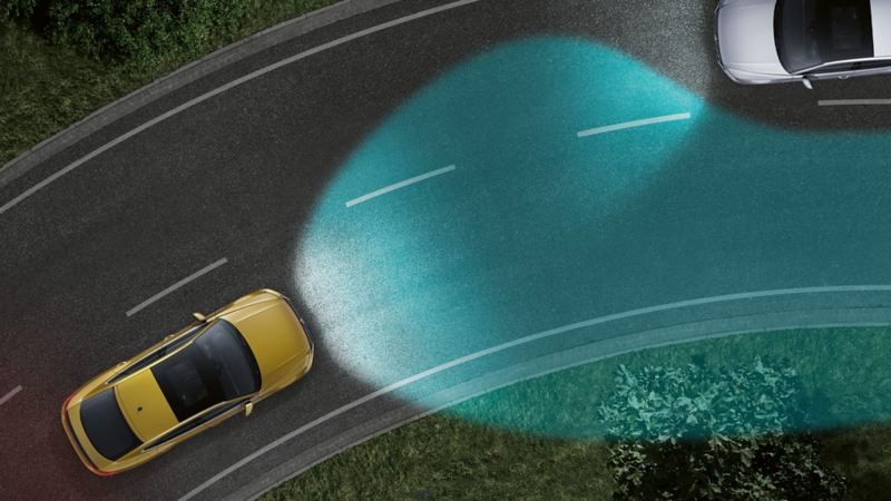 Rappresentazione grafica di un'auto Volkswagen, vista dall'alto, mentre percorre una curva nella notte, con luci di svolta dinamiche attive.