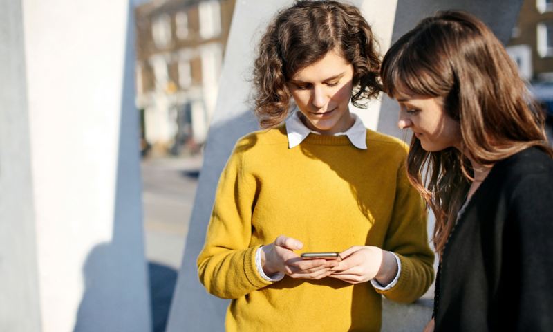 Zwei Frauen blicken zusammen auf ein Smartphone.