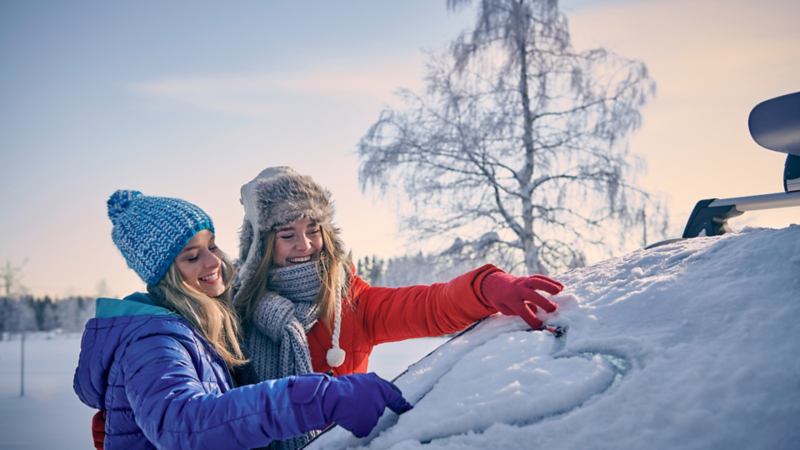 deux filles dessinent avec la neige tombée sur une voiture