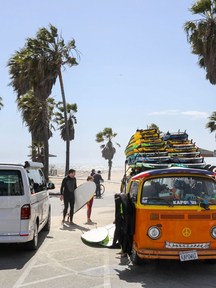 Volkswagen California aan de Californische kust met palmbomen, surfers en surfboards