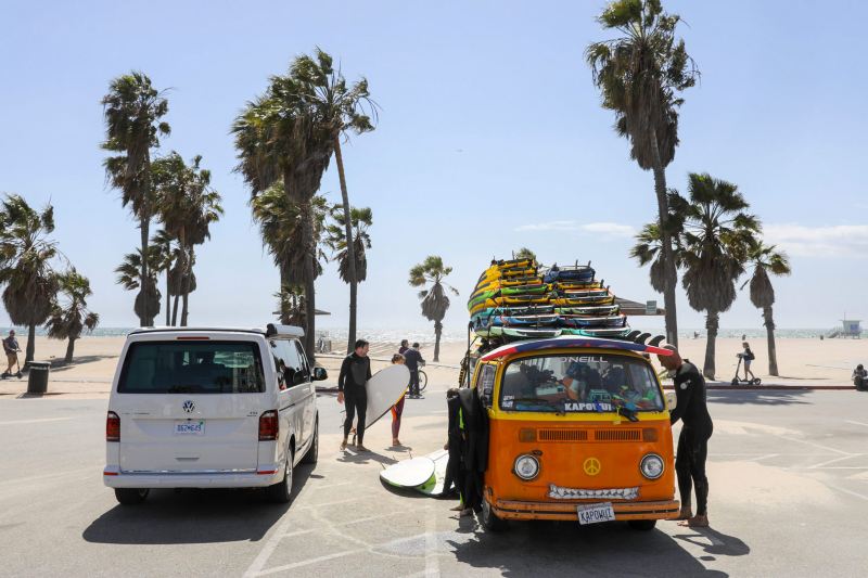 Volkswagen California sur la côte californienne avec palmiers, surfeurs et planches de surf