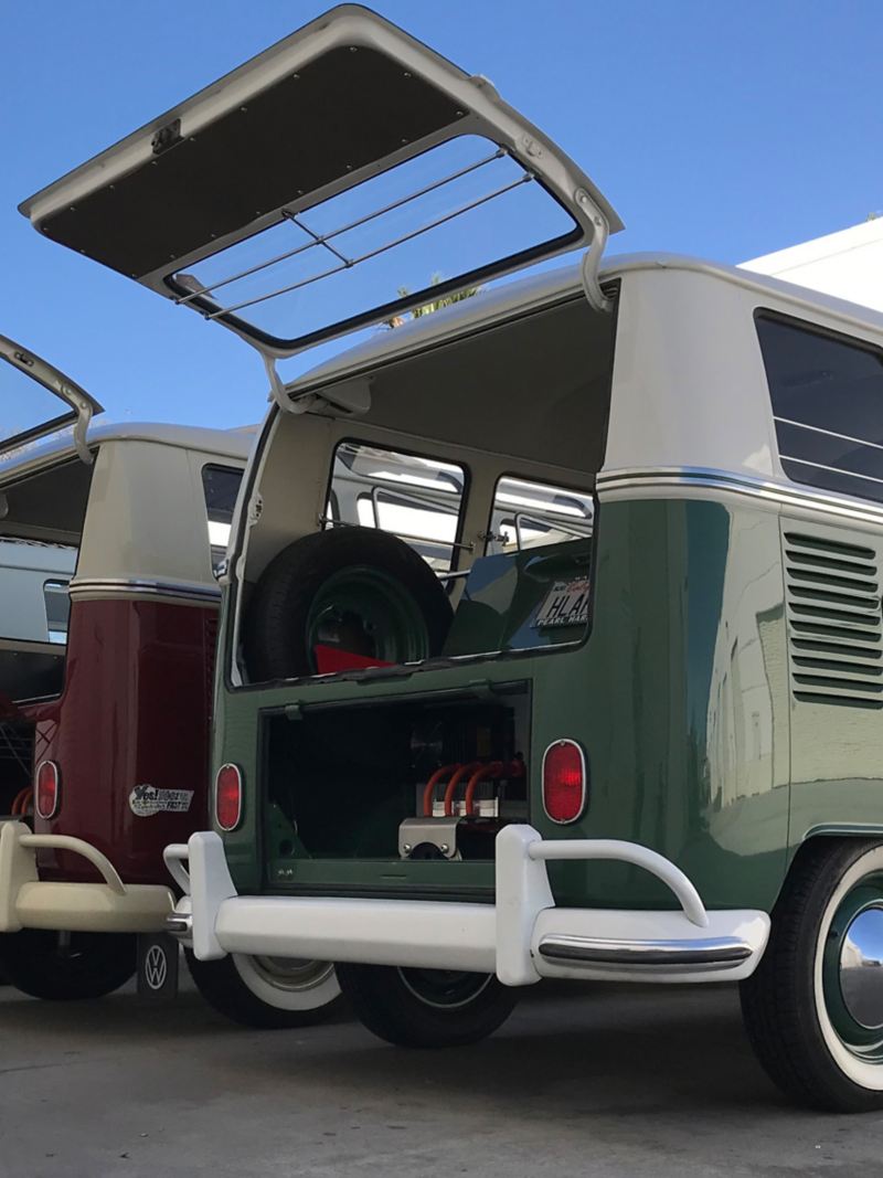 Three VW retro Bullis with electric motors are parked side by side with their boots open.