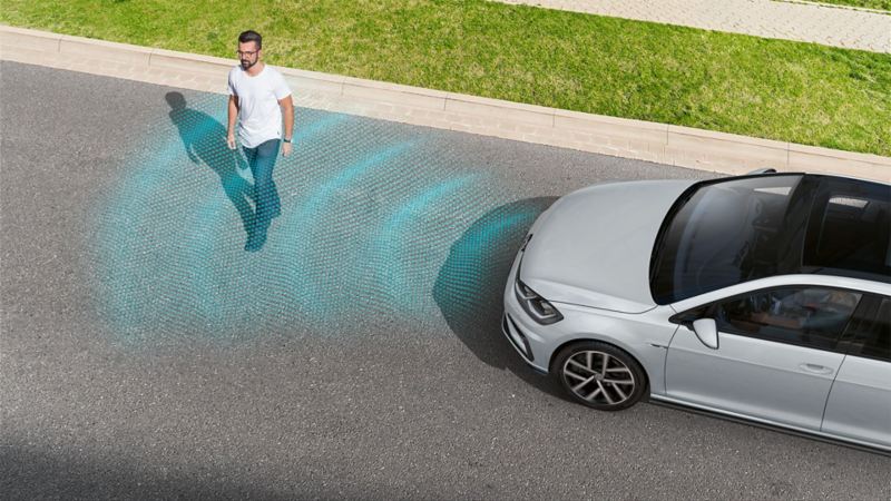A pedestrian crossing the road in front of a VW Golf. The Pedestrian Monitoring sensor system is depicted using lines