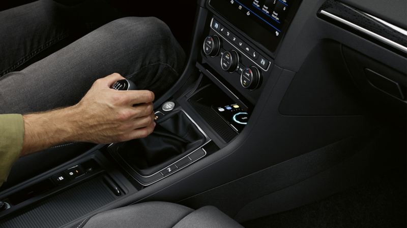 Dettaglio degli interni di un'auto Volkswagen con interfaccia per telefono 'Comfort'; la mano di un uomo è posizionata sulla leva del cambio.