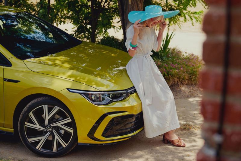 A woman with a white dress stands at the bonnet of the new VW Golf