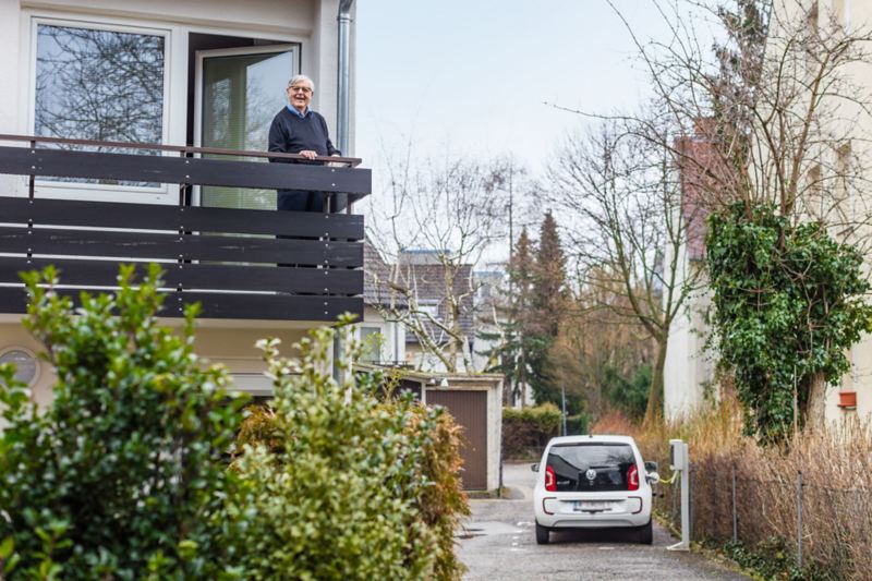 Gerhard Heinz står på sin altan og kigger på sin e-up!, der lader op via wallboxen i gården.