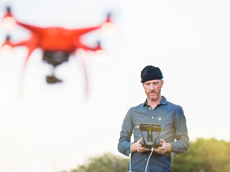 Man flies remote-controlled drone outdoors.