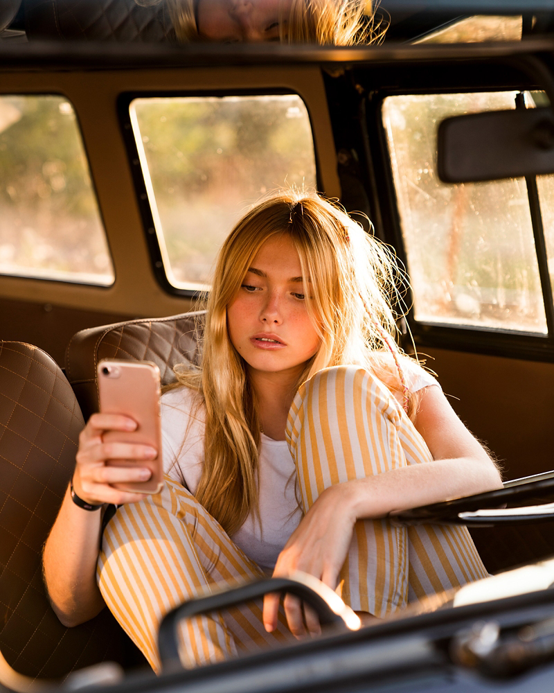 Mujer joven sentada en un coche mirando su teléfono móvil.