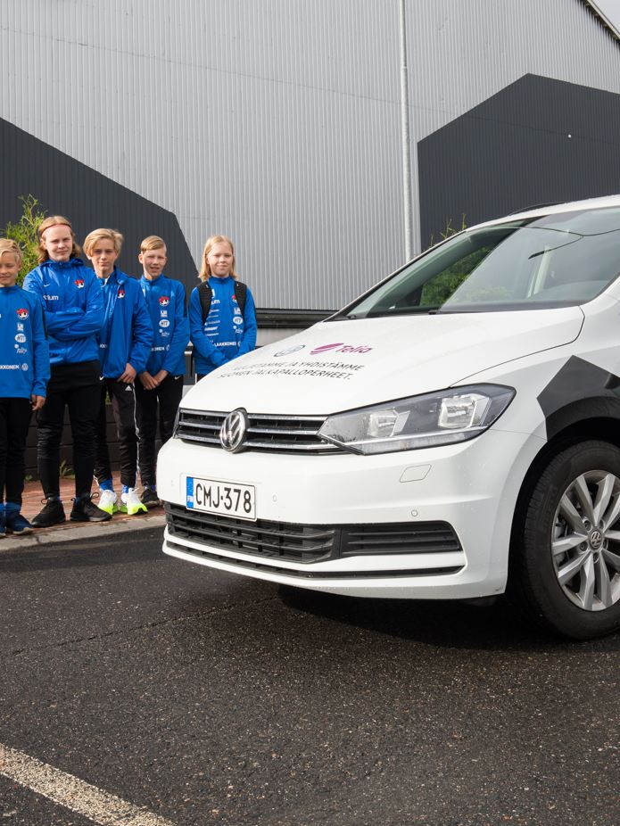 Kuva Volkswagen Touranista ja junioreiden jalkapallojoukkueen pelaajista auton vierellä