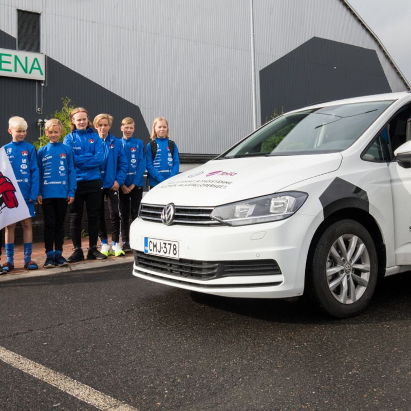 Kuva Volkswagen Touranista ja junioreiden jalkapallojoukkueen pelaajista auton vierellä