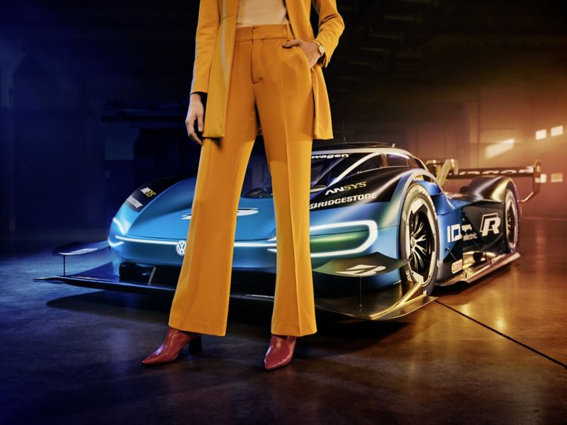 modèle féminin en tailleur pantalon devant la Volkswagen ID.R, voiture de course à propulsion électrique, entrepôt