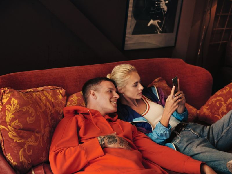 Giovane coppia si sta rilassando su un divano e guardando uno smartphone