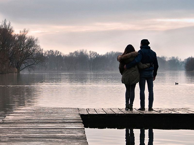 Una coppia abbracciata guarda l'alba in riva a un lago