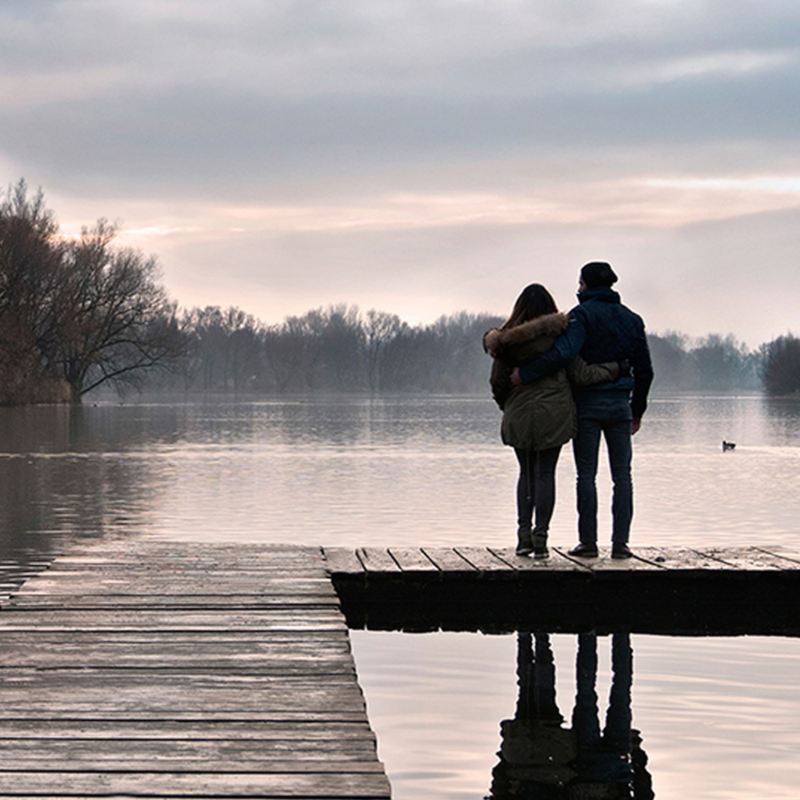 Una coppia abbracciata guarda l'alba in riva a un lago