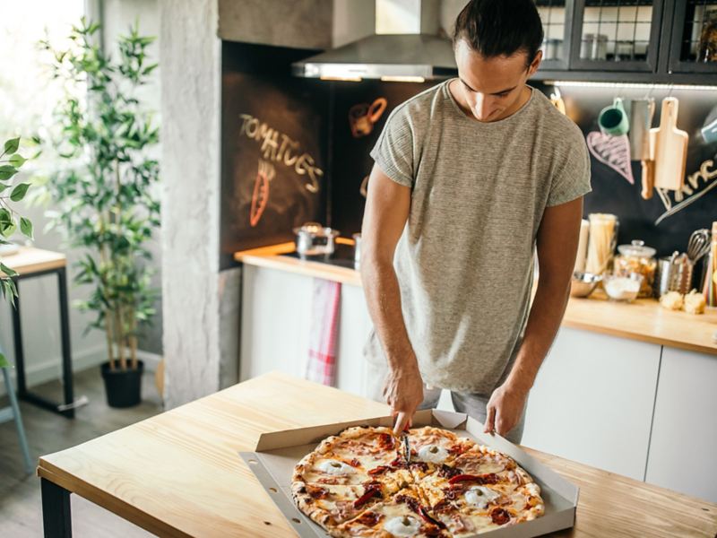 En mand skærer en pizza ud i køkkenet.