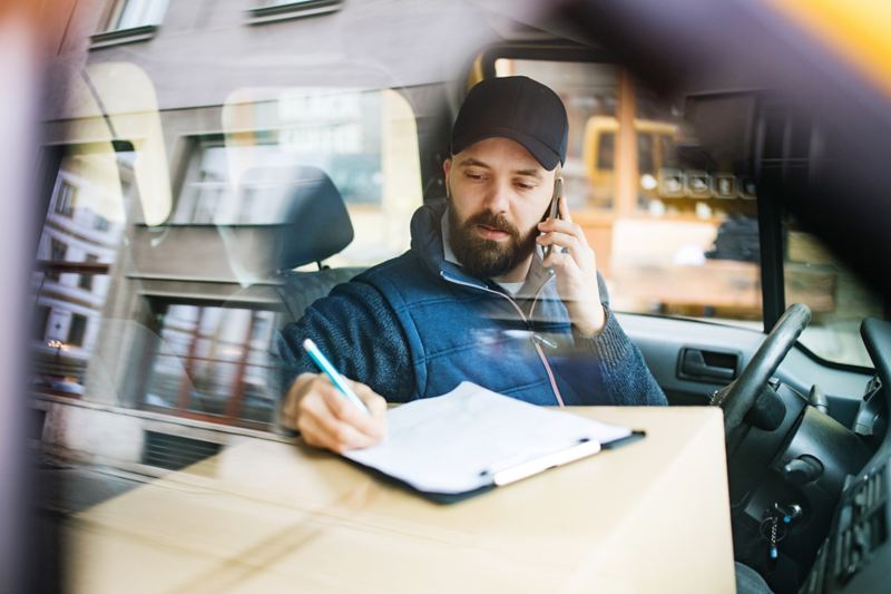 En mand telefonerer i bilen og skriver noget ned.