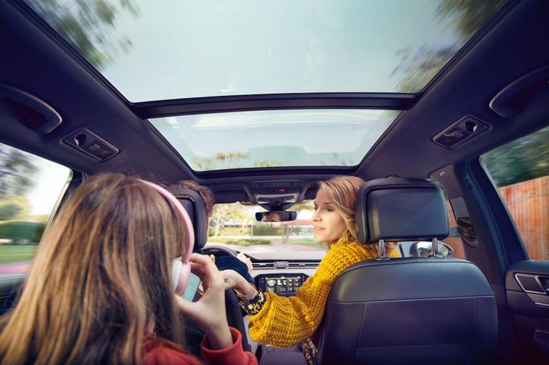 Toit panoramique coulissant/entrebâillant de la Passat, vue vers l’avant depuis le siège arrière, une femme se tourne vers l’enfant qui porte un casque audio