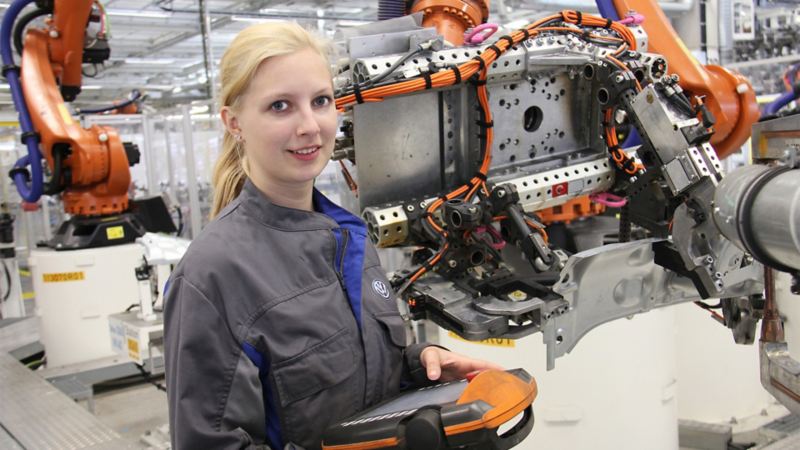 A female Volkswagen employee holding the control unit of an assembly robot