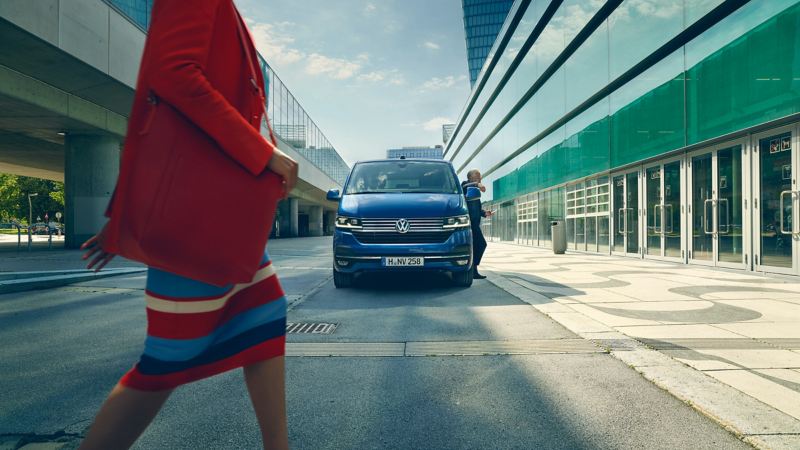 VW Caravelle framfrån med en kvinna i förgrunden, parkerad utanför en flygplats