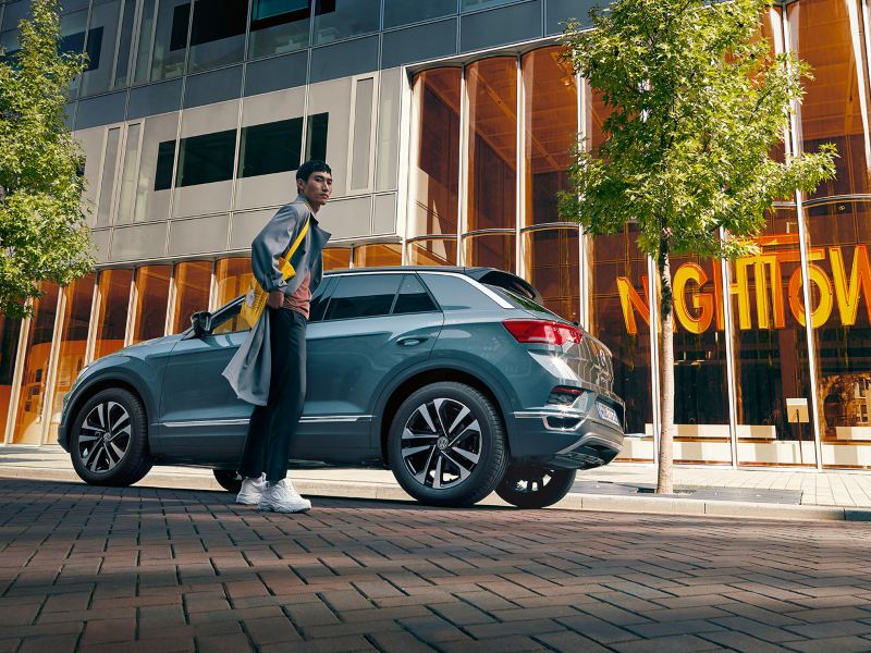 Volkswagen henkilöauto kuvattuna kadulla alaviistosta, auton edustalla seisoo henkilö