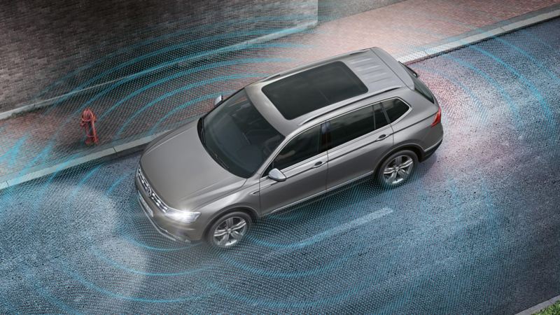 Illustration d’un VW Tiguan Allspace roulant sur une route, les ondes sonores symbolisent les caméras et les capteurs.