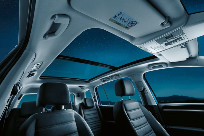 Intérieur du VW Touran à sept places, centré sur le toit ouvrant panoramique en option avec vue sur le ciel étoilé.